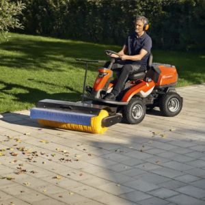 A man using a Husqvarna R 320X AWD Ride On Mower with front-mounted broom attachment